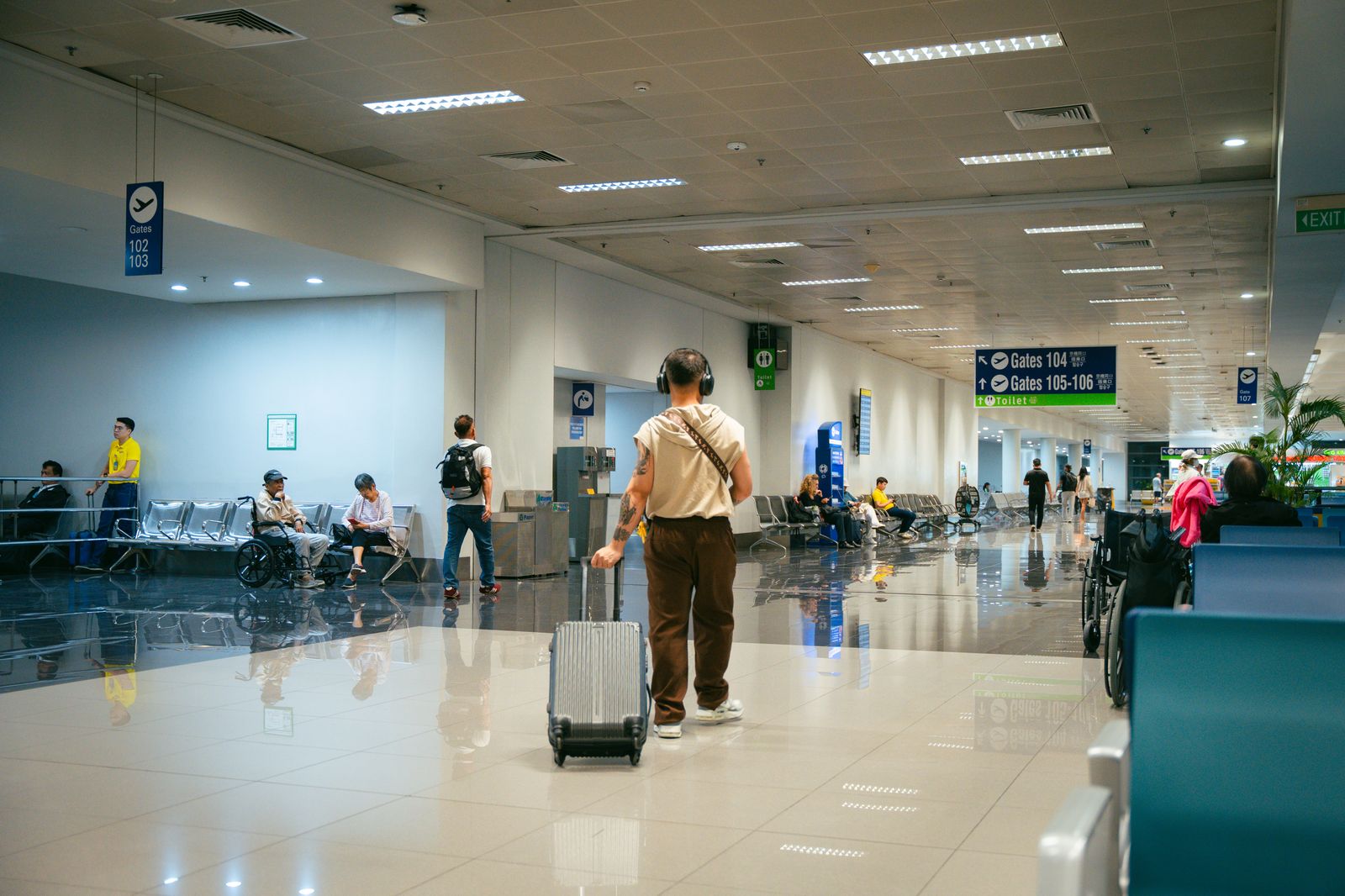 Travellers inside a bright modern airport terminal, including passengers using wheelchairs.